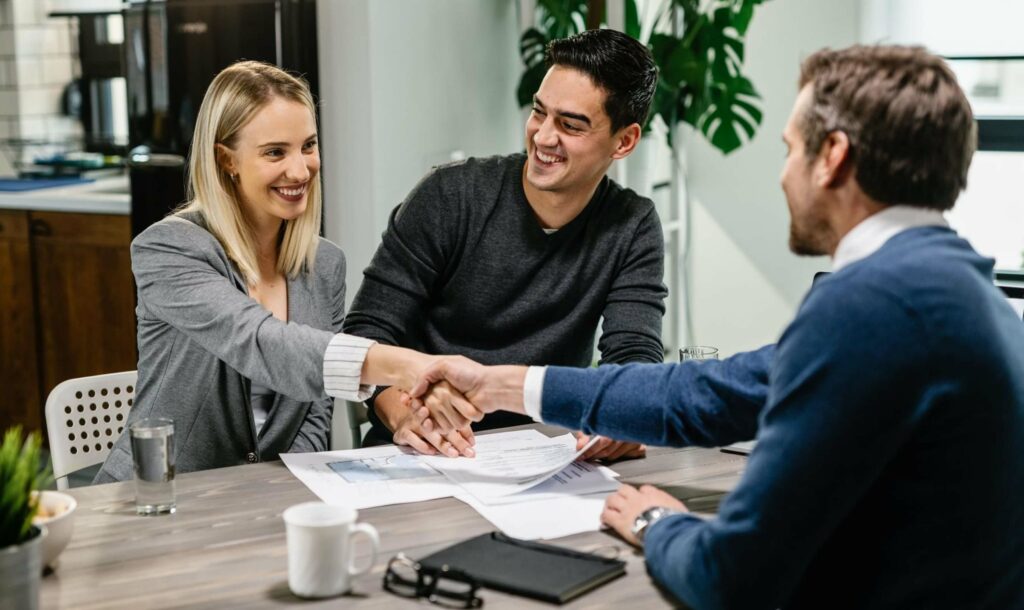 A happy couple shaking hands with a financial advisor during a meeting, symbolising how a comfortable office environment fosters honest discussions for informed decisions.